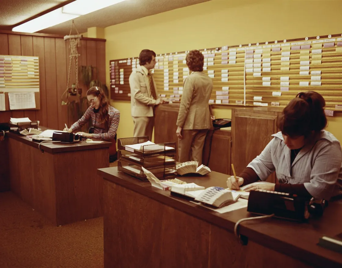 A vintage 1970s office scene with professionals at desks and typewriters, representing older generations who remain active contributors in today’s evolving workforce.