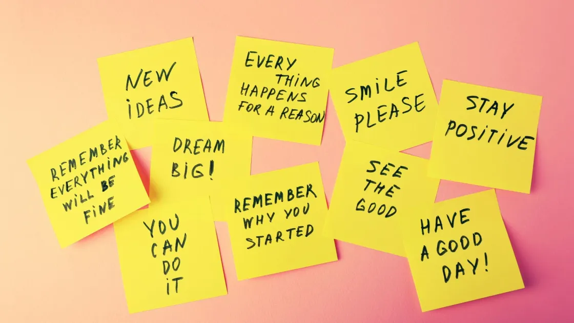 Yellow sticky notes with handwritten motivational phrases like “stay positive,” “dream big,” and “remember why you started,” scattered on a pink background.