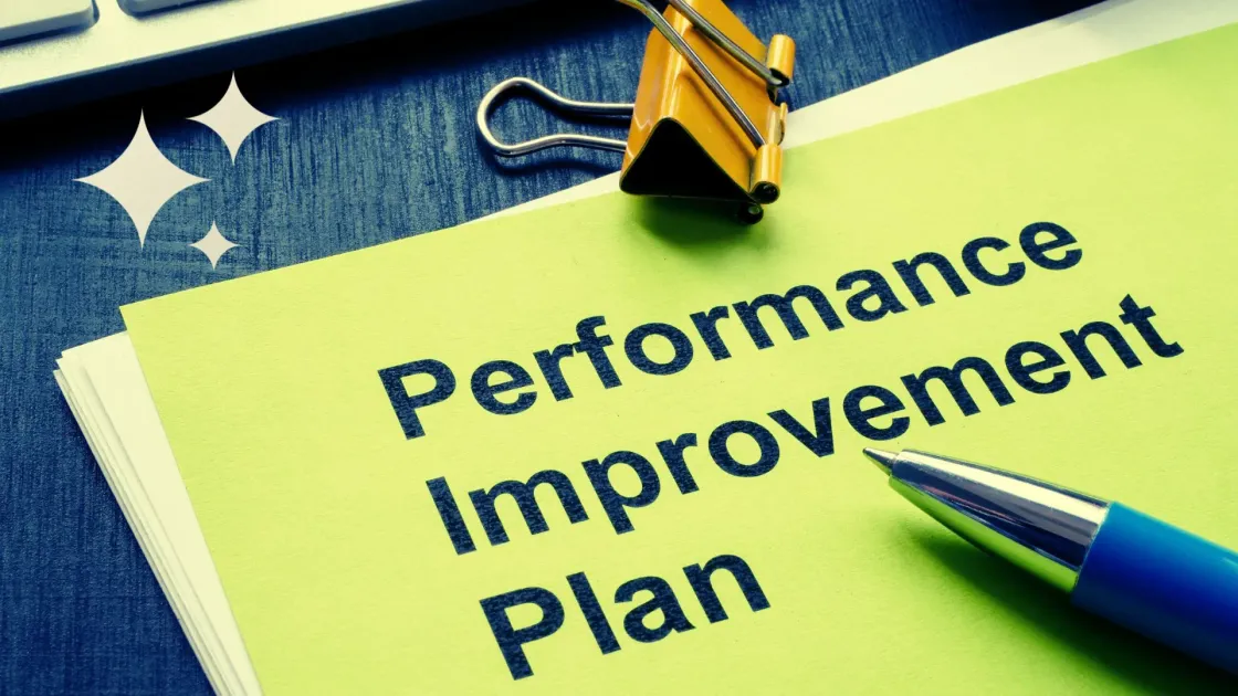 Close-up of a document titled “Performance Improvement Plan” clipped with a binder clip, with a pen pointing at the page on a desk.