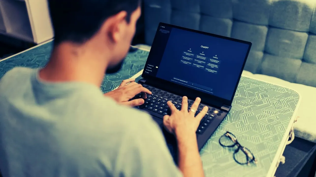 Person typing on a laptop with ChatGPT open on the screen, suggesting AI use at work and extended screen time.