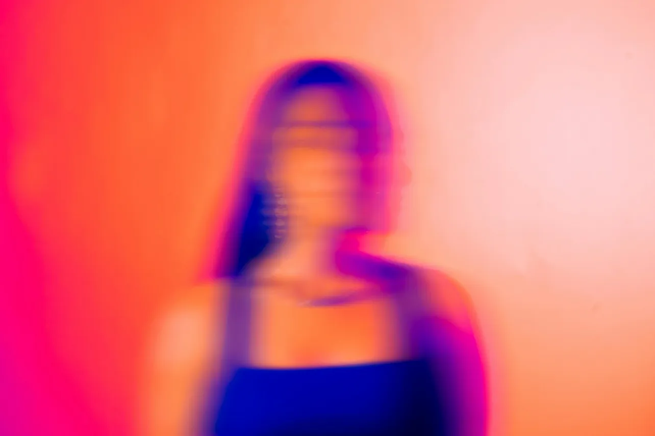 Blurred silhouette of a person in profile against vivid pink, orange and blue light, suggesting uncertainty, identity shift and the human impact of AI at work.